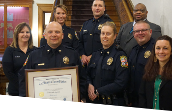A photo of the Chief of Police holding a Certificate of Accreditation next to the Deputy Chief and other police department staff