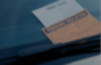 A faded close-up image of a parking ticket paced under the windshield wiper of a vehicle